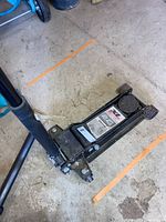 Photo showing a black metal two ton floor jack with padded saddle and label visible on jack body.