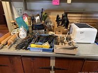 Overview photo showing all items arranged on kitchen counter: toaster, two cutlery blocks, trays of flatware and utensils, rolling pins, oven mitts, bread and cutting boards.