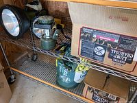 Photo showing large spotlight flashlight, green camp lantern, bag of lump charcoal, and cardboard box with charcoal packaging.