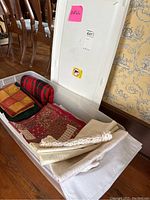 Plastic bin with assorted linens including folded blankets, tablecloth, napkins, placemats