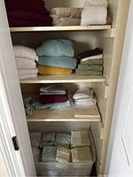 Shelves with stacks of towels and folded linens including various towels in multiple colors and folded bed sheets.