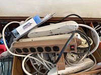 Overview of various power strips, telephones, and electrical cords in a cardboard box.