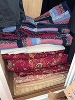 Folded quilts and shams in a storage space, showing patchwork and floral patterns.