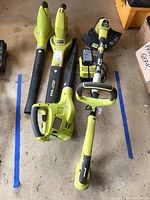 Photo showing three Ryobi leaf blowers and a string trimmer laid out on the floor.