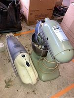 KitchenAid stand mixer with bowl and Filter Stream vacuum placed side by side on a concrete floor with cardboard boxes in background.