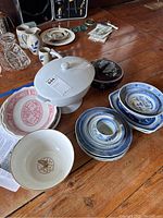 Photo showing assortment of blue and white dishware including bowls, a white casserole dish with lid, and pink/red and blue patterned plates and platters on wooden surface.