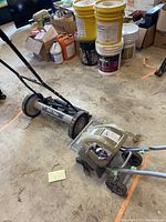 Earthwise tiller and Task Force push reel lawn mower positioned on floor with other household items visible