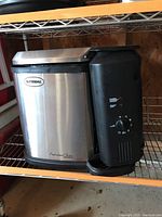 Butterball Professional Series turkey fryer with stainless steel body and black plastic components on wire shelving