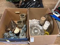 Box with various decorative items including two owl vases, metal fish sculpture, horse head sculpture, covered bird urn, candles in glass holders, hammered metal platter, and glass bowl.