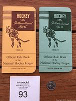 Pair of official NHL rule books from 1962-63 (yellow cover) and 1964-65 (teal cover) placed side by side with a quarter for scale.