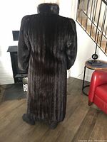 Back view of full length dark brown mink fur coat hanging down to near ankles, showing long straight cut and high collar.