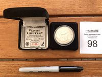 Top view of the opened black presentation box showing the medallion in a plastic holder on one side and the certificate of authenticity on the other.