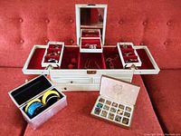 Full view of two vintage jewelry boxes, a small translucent box with bangles, and a vintage purse with accessories inside on an orange background.