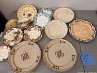 Photo showing various dishes including plates, saucers, cups, and bowl with floral designs arranged on a table.