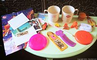 Photo of vintage fast food and cereal premiums on table including mugs, toys, posters and rings
