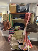 Photo showing various handbags and scarves placed on and around a cream cabinet, with some bags hanging on the sides and scarves draped.