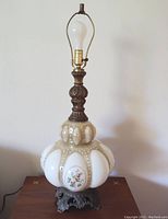 Full view of the lamp showing it unplugged on a table with white opaque glass globe and metal base and stem with patina.