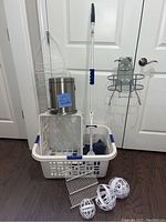 Full lot view showing white Sterilite laundry basket with one handle missing, mop, chrome trashcan, milk crate, iron holder caddy, wire caddies, and bra wash balls arranged together.