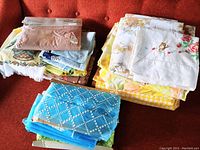 Assorted stacked linens and fabrics including packaged nylon fabric and colorful sheets on an orange fabric couch