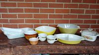 Full group shot of various bowls and casseroles including yellow Pyrex dishes, white casseroles with floral patterns, and mugs.