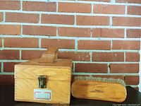 Front view of oak wooden shoe shine box with metal latch, labeled Griffin Shinmaster, sitting beside a Margo horsehair brush