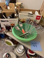 View of Swissmar Sierra fondue set box, Paderno spiral vegetable slicer box, green Tupperware colander, assorted kitchen utensils including whisks, ladle and serving fork
