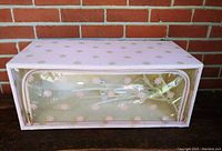 Front view of a rectangular vintage zippered storage box covered in quilted pink vinyl with a clear vinyl front panel printed with a pink floral pattern.