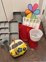 Photo of two Joseph Joseph cutlery organizers, gray and white, colorful pinwheel, wool felt hippie van birdhouse, Glasbake Sunbeam mixing bowl, tin flower pitcher, and red felt bag with handles all grouped together