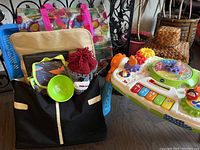 VTech GearZooz Jungle Friends activity table with colorful piano-key buttons and animal figures, next to black Medela Metro diaper bag containing multiple baby items.