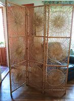Front view of the three-panel wicker screen standing upright showing woven circular starburst patterns and the hinged wooden frame.