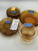 Top view of the brockway plates, vereco shallow bowls, vintage saucers, and the etched footed bowl, showing item sizes on labels and amber color.