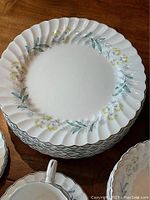 Stack of large dinner plates with visible scalloped edges and yellow, grey, blue floral pattern on white background, platinum trim evident.