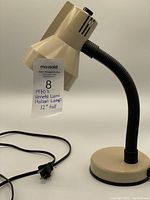 Full view of tan gooseneck desk lamp with black flexible neck and electrical cord with plug.