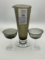 Front view of the retro smoky glass cocktail pitcher placed between two smoky bowl champagne coupe glasses with clear stems.