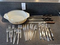 Overview photo showing Pyrex covered dish with lid, arranged flatware including knives and forks, Cutco and Zylco cutting tools.