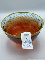 Photo of orange glass bowl with blue swirled decoration, yellow rim, photographed from slightly above showing the bowl's rounded shape and color.