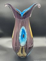 Front view of large art glass vase showing burgundy color with embedded textures and central blue and white floral pattern.