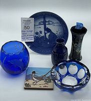 Full lot showing all items: cobalt blue etched Lenox vase, Delft bud vase, W. Germany vase, Royal Copenhagen plate, blue cut glass ashtray, roadrunner tile, and small vases.
