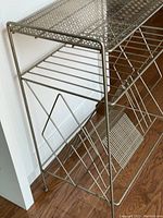 Close-up side angle showing the metal wire lower shelf with angled record dividers and the perforated top shelf.