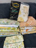 Stack of folded vintage sheets with floral and geometric patterns in yellow, orange, and green hues, laid on dark sofa.