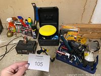 Overview photo showing all items in the car care bundle arranged on the floor, including battery charger, polishing buffer with case, spray bottles, and hand tools.