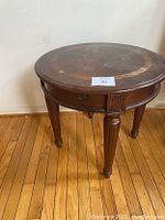 Full view of circular wood side table, showing carved legs and drawer on apron.