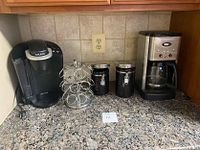 Photo showing all items in the coffee set including Keurig machine, pod rack, two canisters, and Cuisinart drip coffee maker on a granite countertop.
