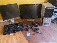 Photo showing two flat screen monitors, two keyboards, two mice, one headset, a computer tower, and assorted cords on a table.