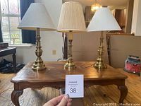 Three gold-tone table lamps placed on a wooden table, each with a different lampshade. Used condition, visibly clean.