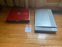 Closed laptop and Epson flatbed scanner placed on wooden floor.