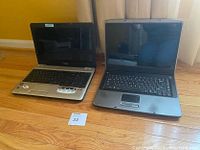 Front view of two laptops showing open screens and keyboards on wooden floor with yellow wall background. Toshiba and Gateway brands visible.