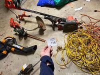 Overview showing 2 Black & Decker trimmers, Black & Decker Edge Hog attachment, WORX leaf blower, and tangled extension cord on floor.