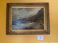 Frontal image showing the oil painting that depicts a rocky coastline with waves and a cloudy sky, set in an ornate gold frame with visible minor chips.