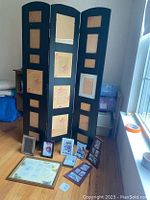 Photo of 3-panel standing frame with multiple photo slots, six 4x6 frames and collage frames arranged at base, unopened condition.